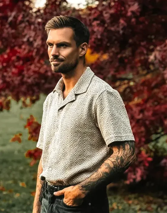 Homme avec tatouages devant des arbres.